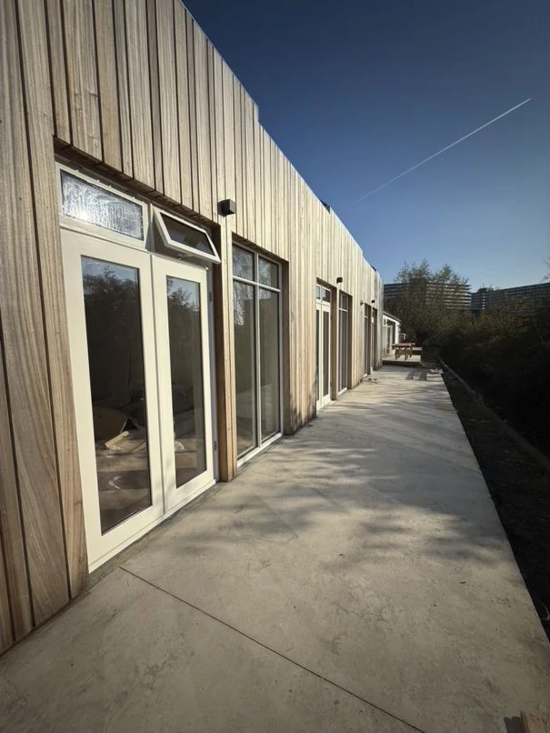 Verticale houten bekleding, grote kozijnen en een doorlopende aansluiting op het terras.